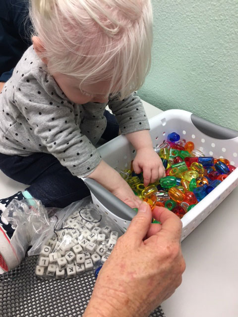 A child is digging through colorful beads to attach to the tactile story board